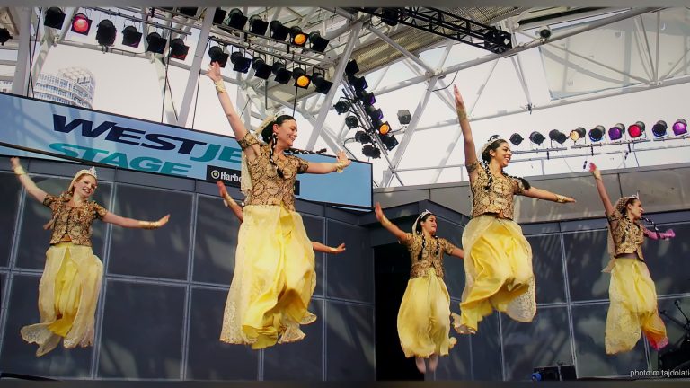 Dancers in yellow skirts leaping on the WestJet Stage, Tirgan 2013