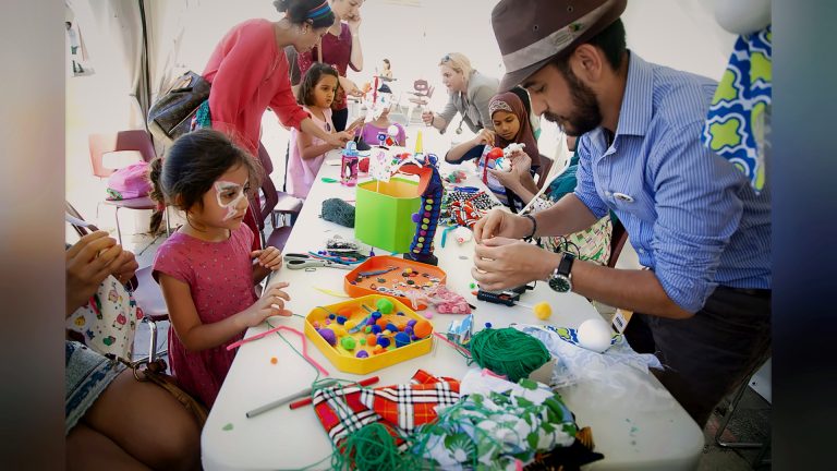 Children making crafts with a volunteer in the kids' tent, Tirgan 2015