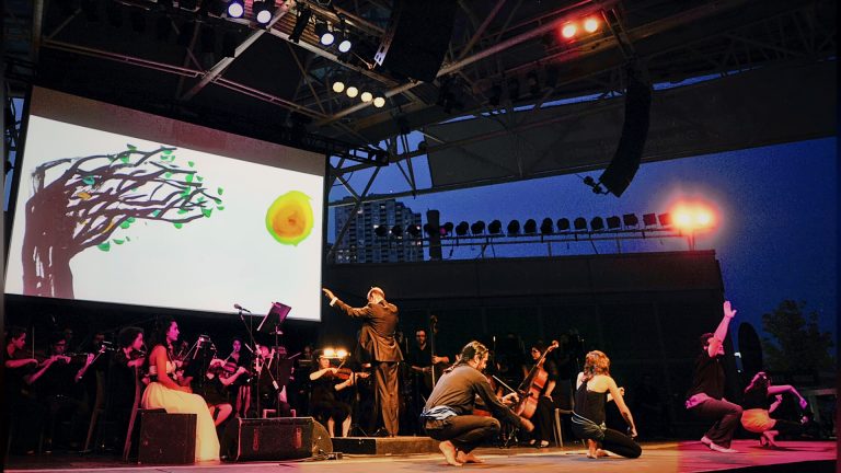Orchestra and dancers performing on the outdoor stage at dusk, Tirgan 2013
