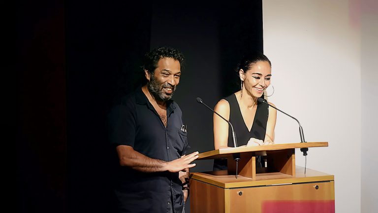 Two presenters speaking at a podium, Tirgan 2013